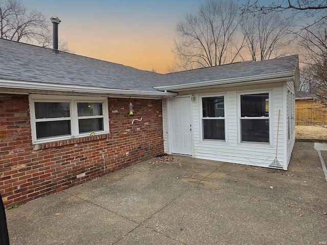 back of house with a shingled roof, brick siding, and a patio