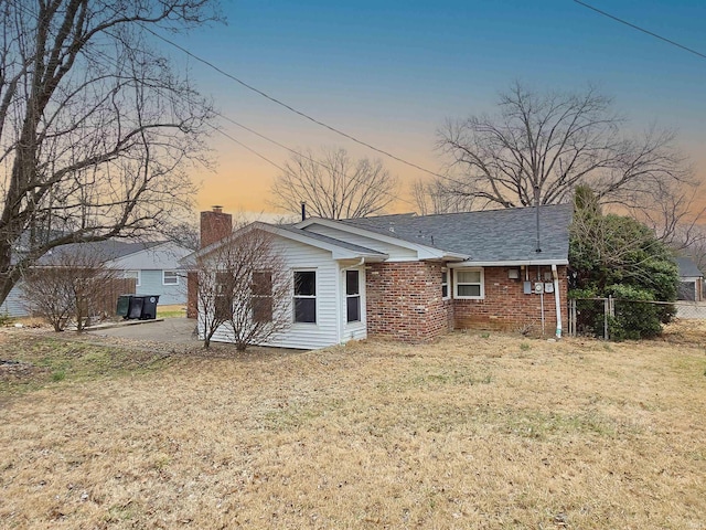 rear view of house with brick siding, a chimney, fence, and a lawn