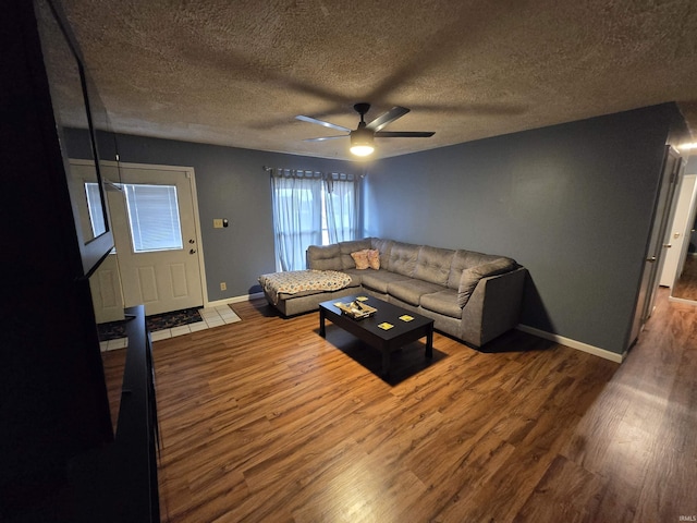 living area featuring a ceiling fan, a textured ceiling, baseboards, and wood finished floors