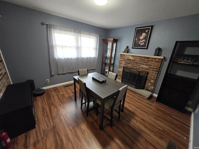 dining space featuring visible vents, a fireplace, baseboards, and wood finished floors