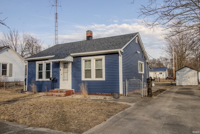 bungalow featuring a garage, a storage shed, a chimney, an outbuilding, and roof with shingles