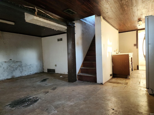 finished below grade area featuring freestanding refrigerator, wooden ceiling, visible vents, and stairs