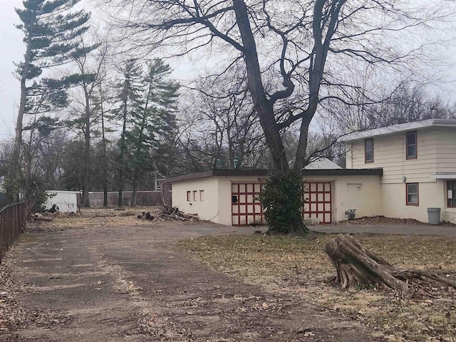 exterior space featuring dirt driveway, an attached garage, and fence