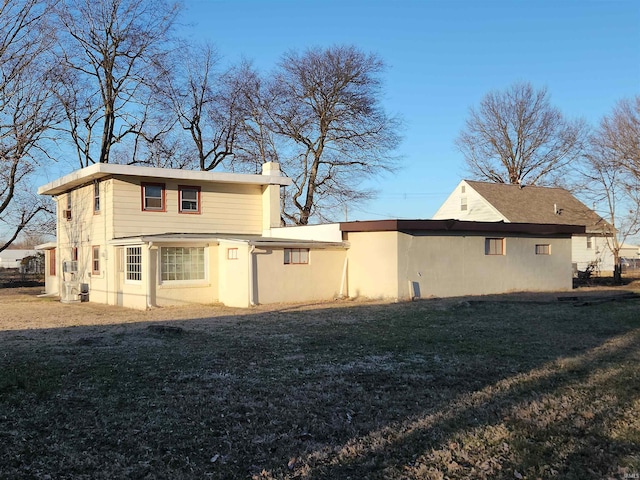 rear view of property with stucco siding, a chimney, and a yard