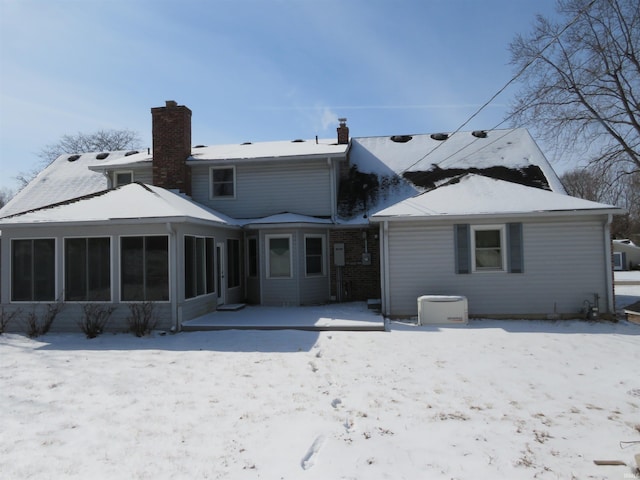 snow covered rear of property with a sunroom and a chimney