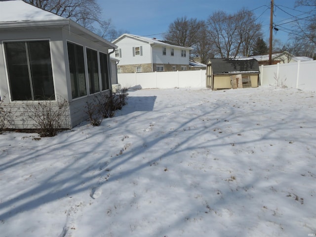 snowy yard with a sunroom, a fenced backyard, a shed, and an outbuilding