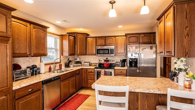 kitchen with stainless steel appliances, tasteful backsplash, light wood-style flooring, a sink, and a peninsula