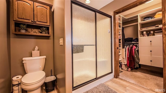 bathroom featuring a stall shower, wood finished floors, toilet, and a walk in closet