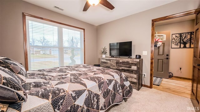 bedroom featuring baseboards, visible vents, light colored carpet, light wood-style flooring, and ceiling fan