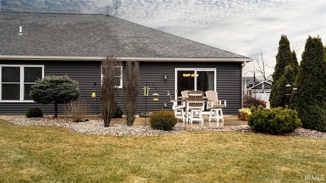 rear view of property featuring roof with shingles, a patio, and a lawn