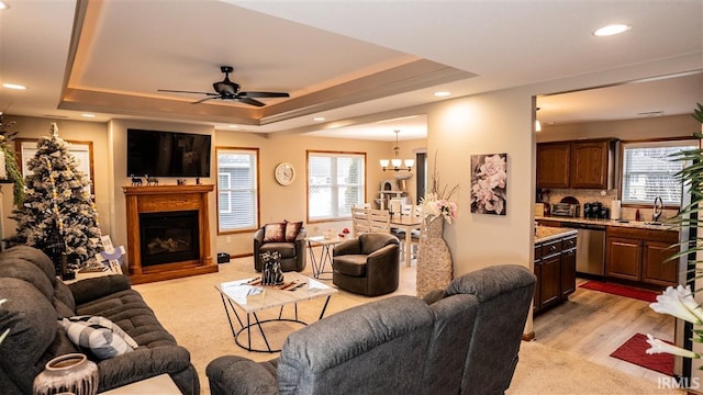 living room with recessed lighting, light wood-style flooring, a tray ceiling, a fireplace, and ceiling fan with notable chandelier