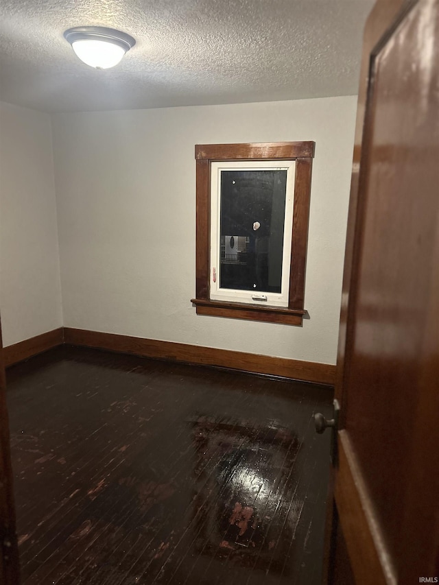 spare room with dark wood-style floors, a textured ceiling, and baseboards