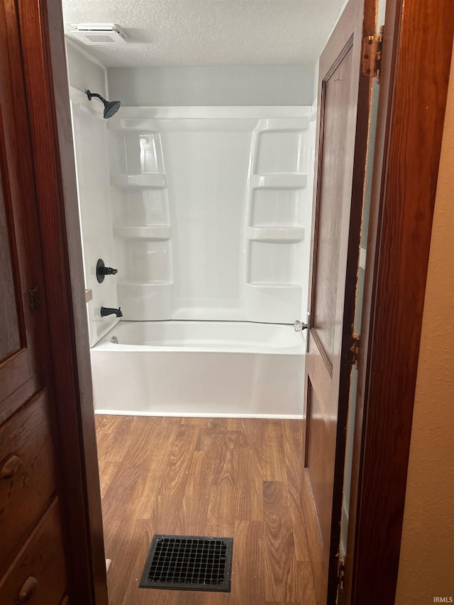 bathroom with washtub / shower combination, visible vents, a textured ceiling, and wood finished floors