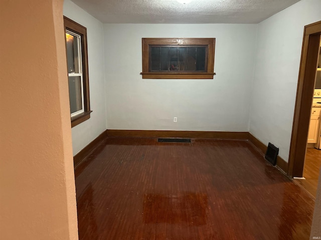 spare room featuring a textured ceiling, wood finished floors, visible vents, and baseboards