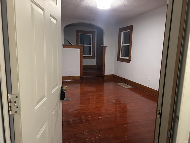 hallway with arched walkways, dark wood finished floors, a textured ceiling, baseboards, and stairs