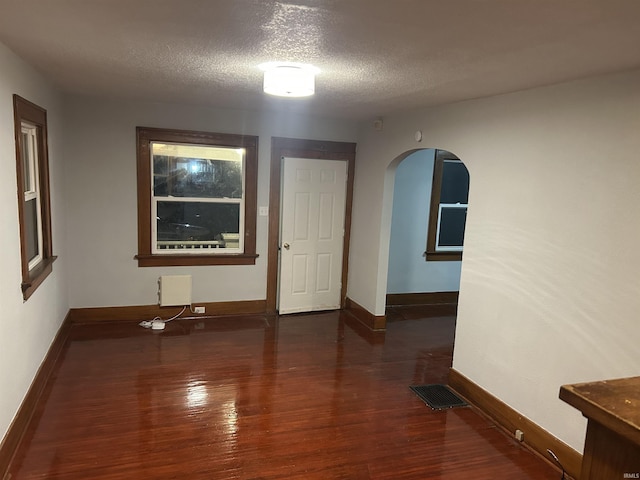 empty room featuring arched walkways, visible vents, a textured ceiling, and wood finished floors