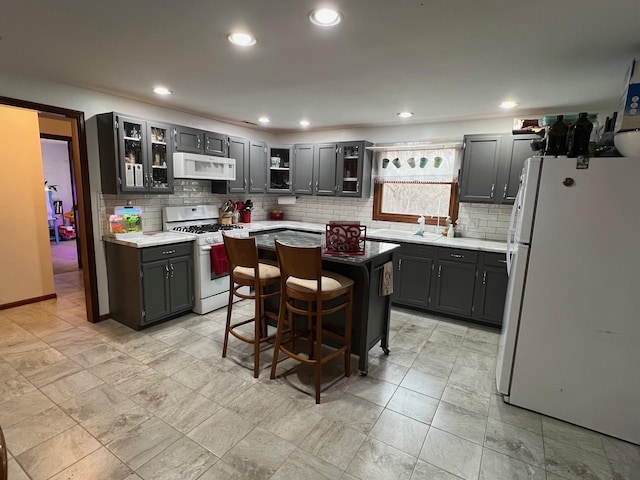 kitchen with recessed lighting, white appliances, a center island, tasteful backsplash, and glass insert cabinets