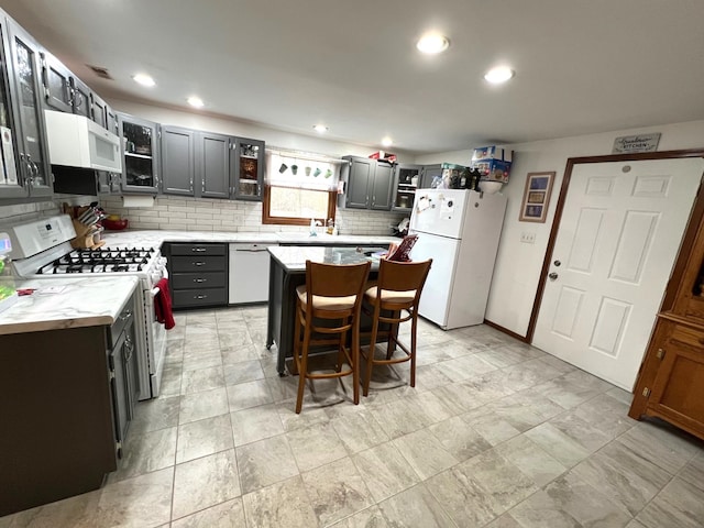 kitchen featuring a breakfast bar, a center island, light countertops, backsplash, and white appliances