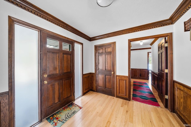 entryway featuring light wood-style floors, ornamental molding, and wainscoting