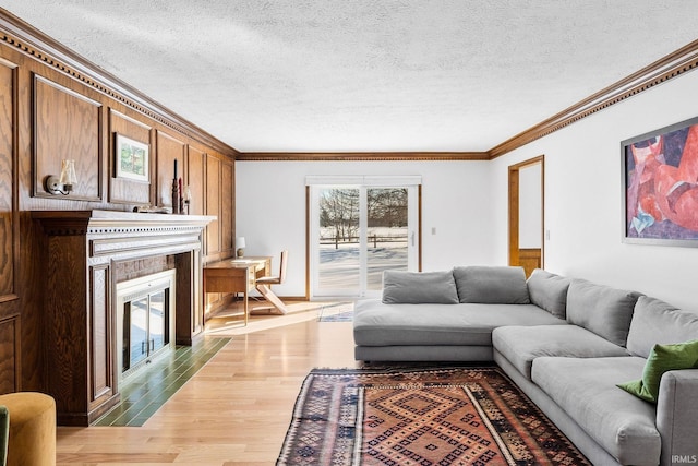 living area with a textured ceiling, wood finished floors, a fireplace with flush hearth, and crown molding