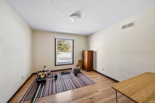 exercise area with visible vents, light wood-style flooring, baseboards, and a textured ceiling