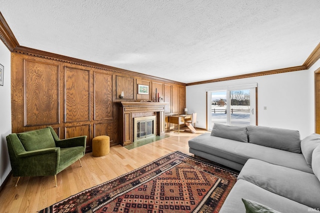 living area with a fireplace with flush hearth, crown molding, a textured ceiling, and light wood finished floors