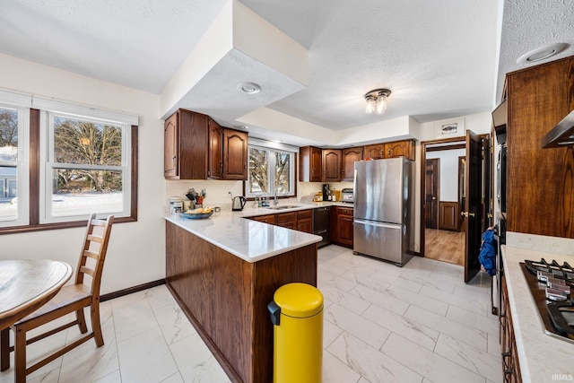 kitchen featuring appliances with stainless steel finishes, a peninsula, marble finish floor, light countertops, and a sink