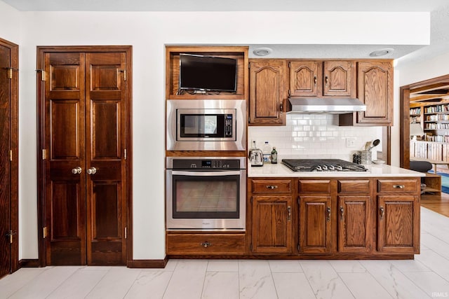 kitchen with under cabinet range hood, light countertops, appliances with stainless steel finishes, marble finish floor, and tasteful backsplash