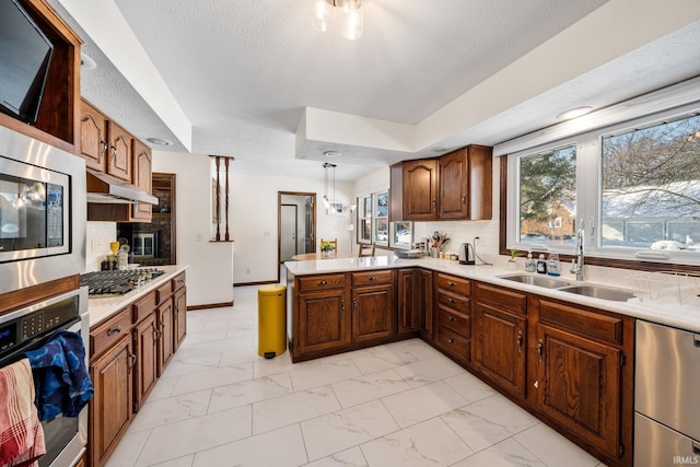 kitchen with appliances with stainless steel finishes, a peninsula, marble finish floor, under cabinet range hood, and a sink