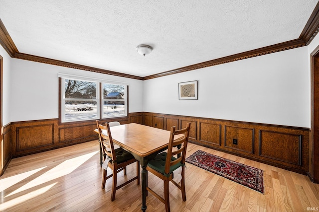 dining space with a wainscoted wall, a textured ceiling, and light wood-style floors