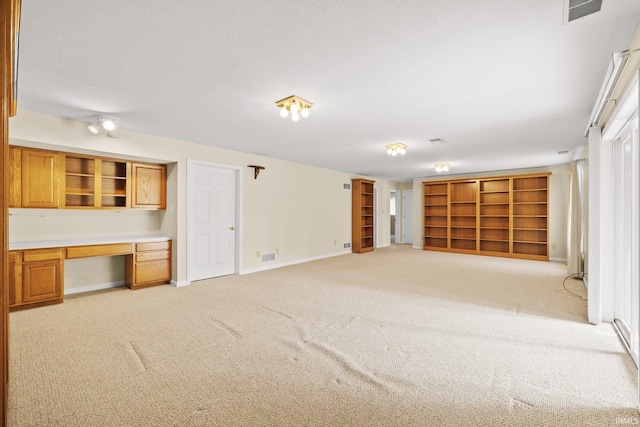 unfurnished living room with visible vents, light carpet, built in desk, and baseboards