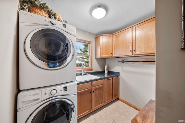 laundry area with cabinet space, light tile patterned floors, baseboards, stacked washer and clothes dryer, and a sink