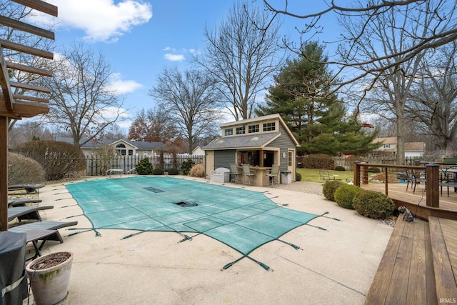 view of pool with outdoor dry bar, fence, a deck, an outdoor structure, and a storage structure