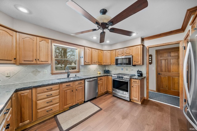 kitchen with tasteful backsplash, appliances with stainless steel finishes, dark stone countertops, wood finished floors, and a sink