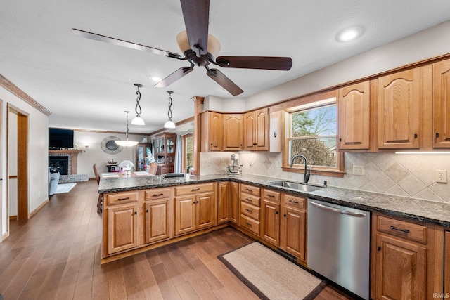 kitchen with dark wood-style flooring, stainless steel dishwasher, a brick fireplace, a sink, and a peninsula