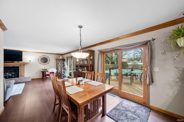 dining space with hardwood / wood-style flooring, a brick fireplace, baseboards, and crown molding