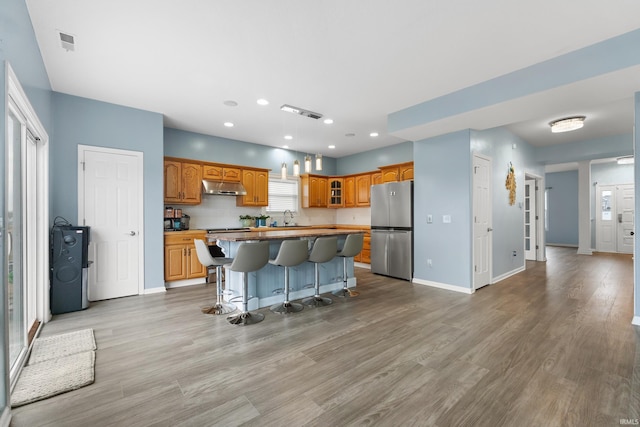 kitchen with freestanding refrigerator, a kitchen island, under cabinet range hood, and light wood finished floors