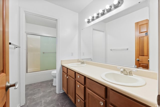 full bathroom featuring double vanity, shower / bath combination with glass door, a sink, and toilet