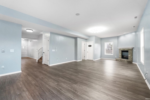 unfurnished living room featuring dark wood-type flooring, stairway, a brick fireplace, and baseboards