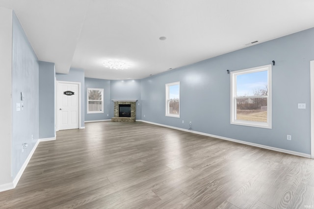 unfurnished living room with a brick fireplace, visible vents, baseboards, and wood finished floors