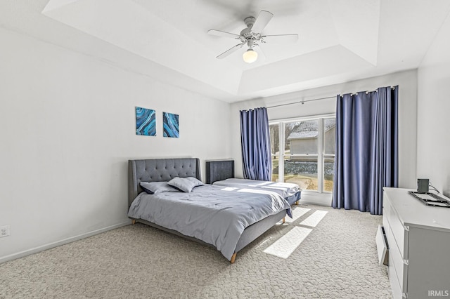 bedroom featuring light carpet, baseboards, a tray ceiling, and a ceiling fan