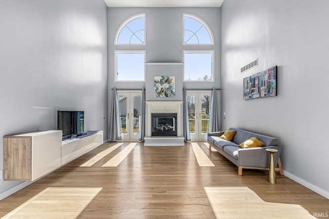 living area featuring baseboards, visible vents, a glass covered fireplace, wood finished floors, and french doors