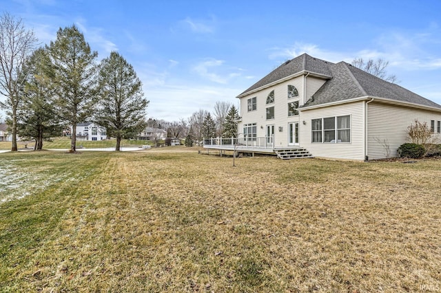 back of property featuring a deck, roof with shingles, and a lawn