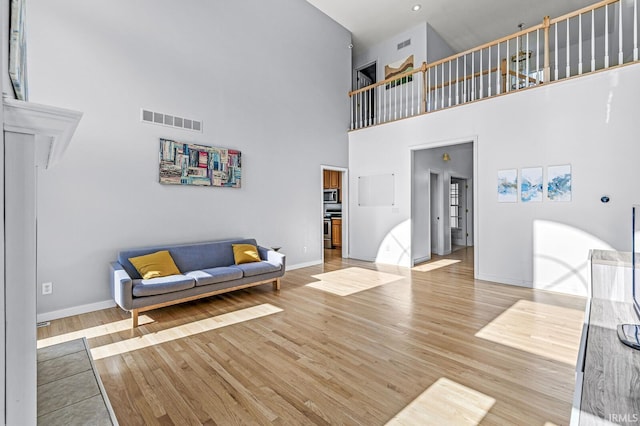 living room with a towering ceiling, visible vents, light wood-style flooring, and baseboards