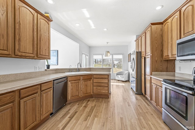 kitchen with a peninsula, appliances with stainless steel finishes, a sink, and brown cabinets