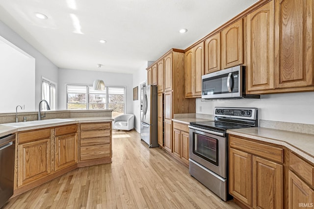 kitchen with stainless steel appliances, brown cabinetry, a sink, and light wood-style floors