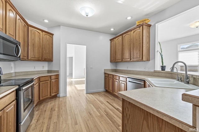 kitchen featuring appliances with stainless steel finishes, light wood-type flooring, a sink, and brown cabinets