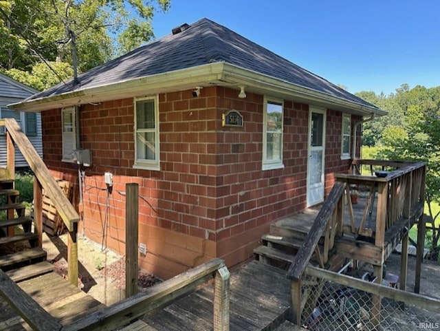 view of side of home featuring a deck, brick siding, and roof with shingles