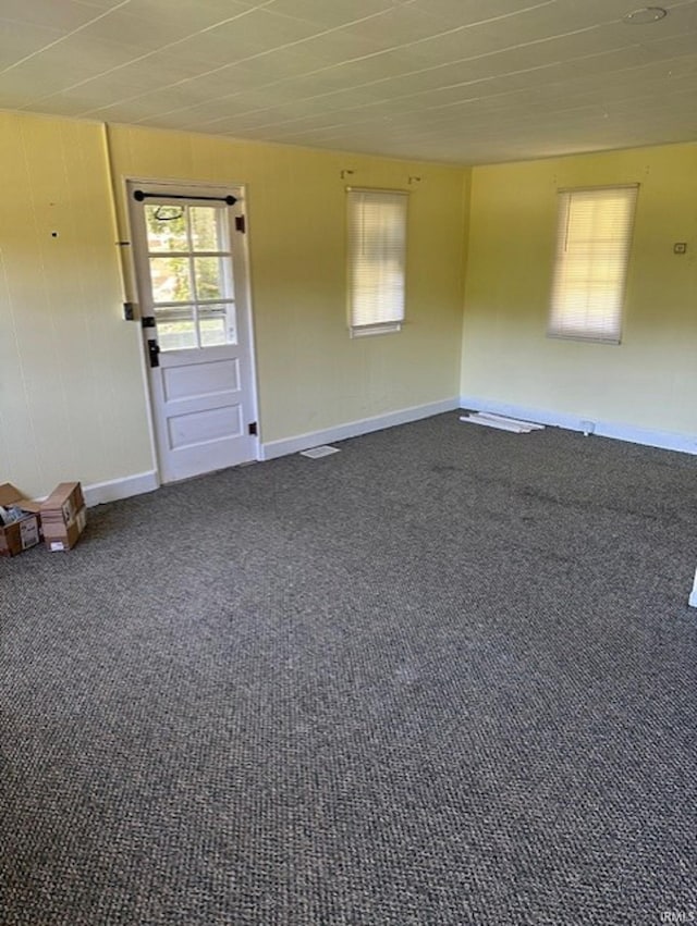 empty room with dark colored carpet, visible vents, and baseboards