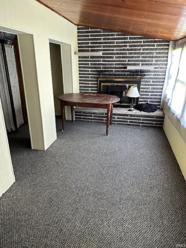 interior space featuring vaulted ceiling, carpet flooring, a glass covered fireplace, and wood ceiling